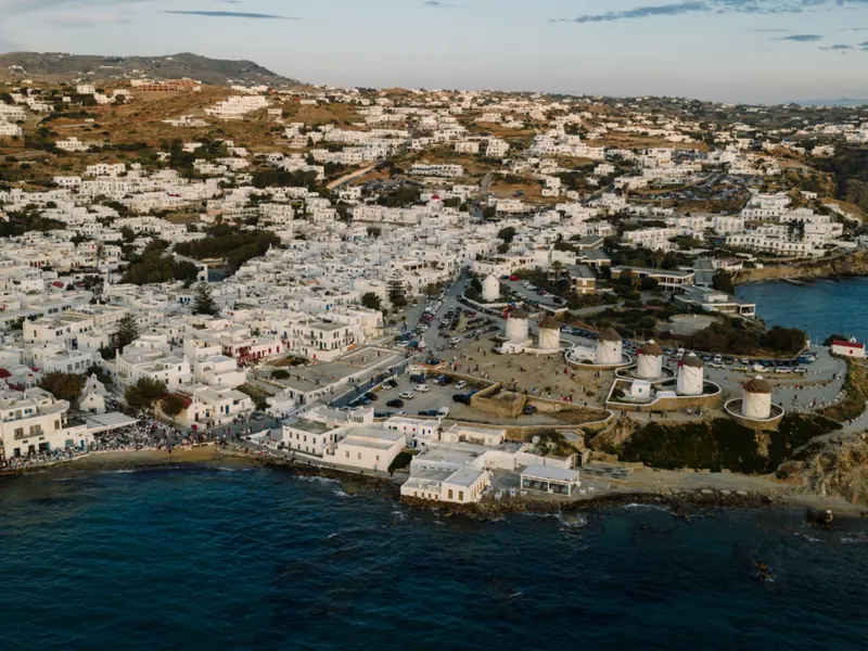 Luchtfoto van Mykonos-stad met witte huizen, traditionele windmolens en uitzicht op de Egeïsche Zee.